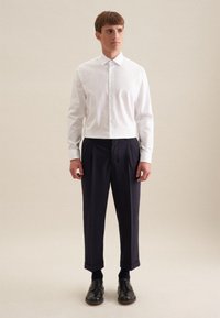 Weißes Hemd mit Knopfverschluss, kombiniert mit navy-blauen, gefalteten Hosen mit geradem Bein und schwarzen Dressschuhen. Einfarbig, minimalistische Details.