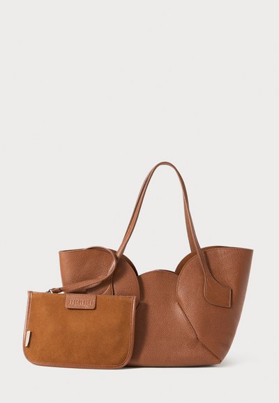 Braune Leder-Tasche mit gewellten Kanten und passendem Wildleder-Handgelenkbeutel mit Reißverschluss auf einem weißen Hintergrund.