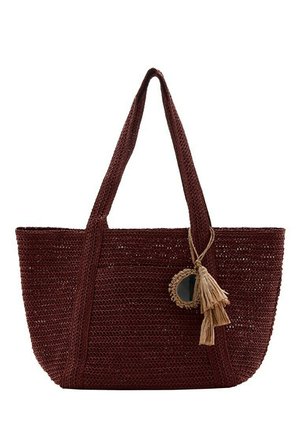 Sac cabas tissé marron foncé avec deux longues anses, avec un miroir rond décoratif et un pompon beige suspendu à une anse.