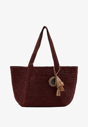 Bolso tote tejido de color marrón oscuro con dos asas largas, que presenta un espejo redondo decorativo y un adorno de borla beige colgando de una de las asas.