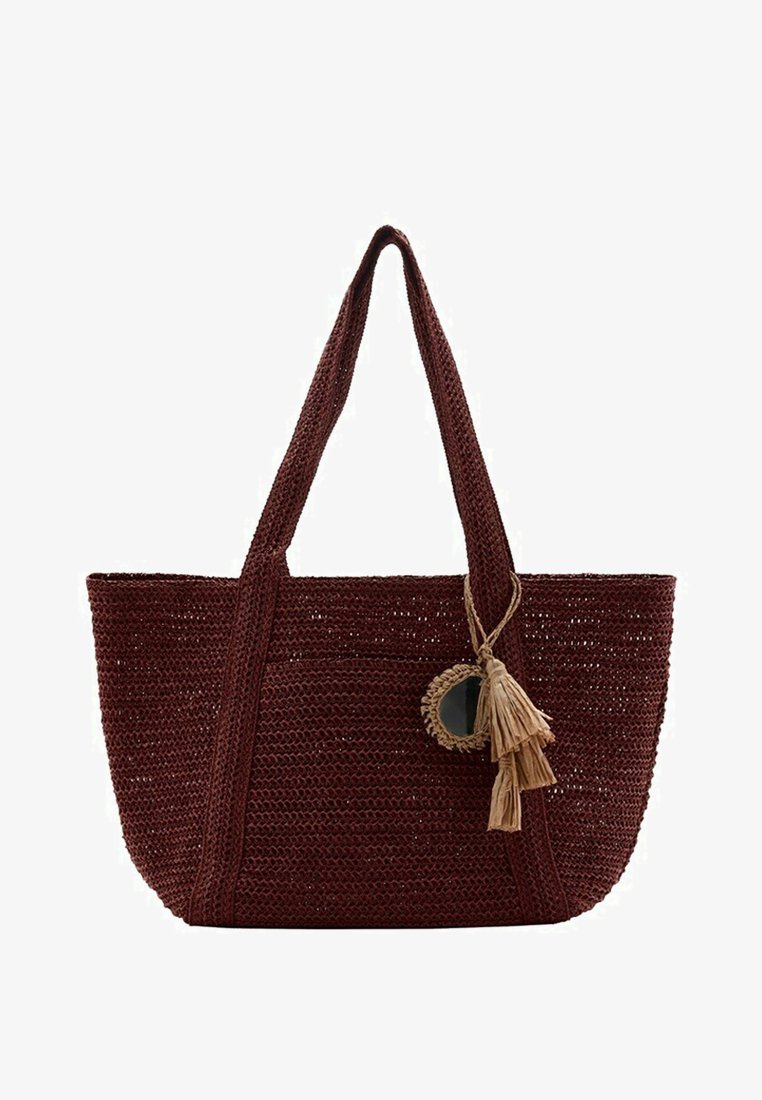 Sac cabas tissé marron foncé avec deux longues anses, avec un miroir rond décoratif et un pompon beige suspendu à une anse.