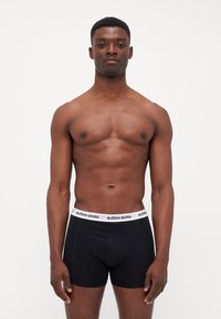 Sorte boxershorts laget av myk stoff med en hvit elastisk midjebånd som har "BJÖRN BORG" merkevare. Passformen er tettsittende og formet.