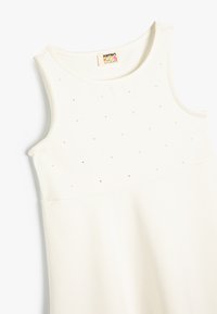 Vestido sin mangas color crema con cuello redondo, adornado con pequeños strass en el corsé y con una textura de tela suave.