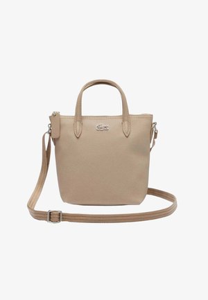 Sac bandoulière en tissu beige texturé avec deux poignées, sangle réglable, fermeture éclair et petit logo crocodile à l'avant.