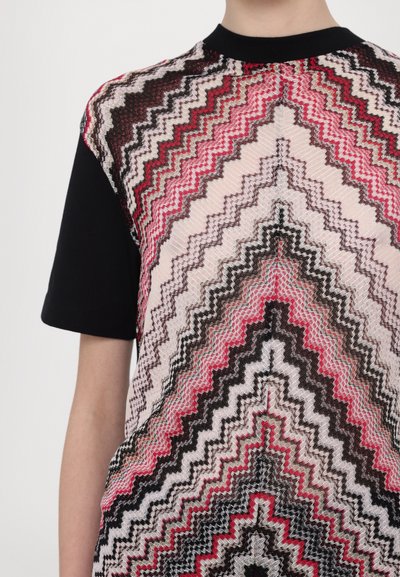 Camiseta de manga corta con un patrón en zigzag en rosa, negro y crema, que presenta tela negra en las mangas y el cuello.