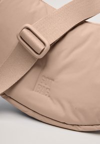 Borsa a tracolla beige realizzata in morbido materiale imbottito, con una tracolla texturizzata e un logo "GOT BAG" impresso.