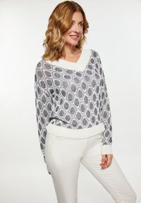 Könnyű kötött pulóver fehér színben, sötétkék ovális mintával. V-alakú nyakkivágással és bordázott szegéllyel rendelkezik. Fehér, slim-fit nadrággal párosítva.