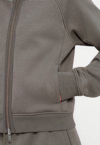 Γκρι ζακέτα με φερμουάρ και υφή, με όρθιο γιακά, ριμπ μανσέτες και μεταλλικό φερμουάρ. Διαθέτει πλαϊνές τσέπες.