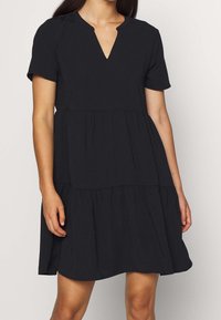 Black dress with short sleeves, a V-neck, and tiered design. Made of soft fabric with a flowing silhouette for comfort and ease of movement.