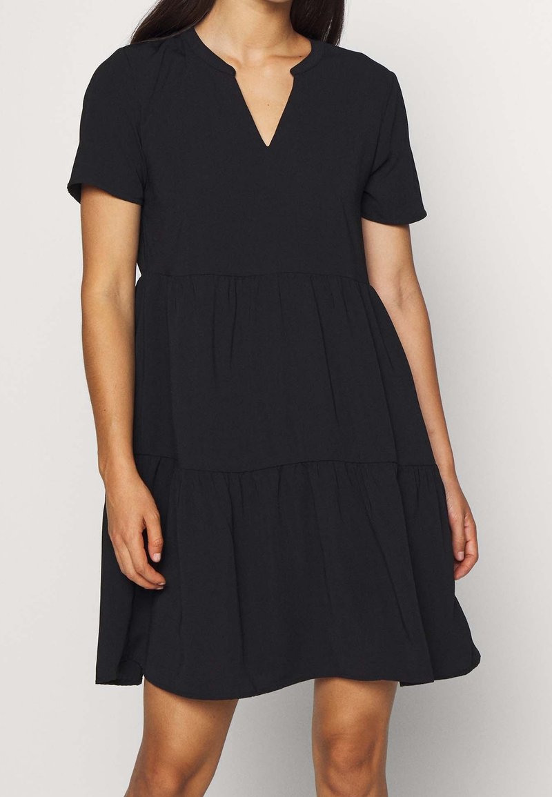 Black dress with short sleeves, a V-neck, and tiered design. Made of soft fabric with a flowing silhouette for comfort and ease of movement.