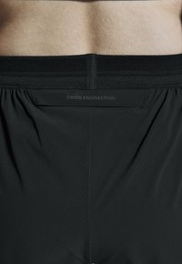 Zwarte sportshorts met een geperforeerd ontwerp, een brede elastische tailleband en de tekst "SWISS ENGINEERING" subtiel op de achterkant gedrukt.
