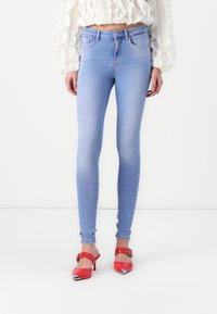 Ljusblå skinny jeans i denim med en klassisk femfickdesign, bärs med röda klackskor med metalliska detaljer.