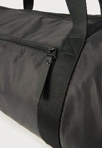 Μαύρη τσάντα duffel από νάιλον με φερμουάρ, ενισχυμένους μαύρους ιμάντες, λεία υφή και διακριτικές ραφές.