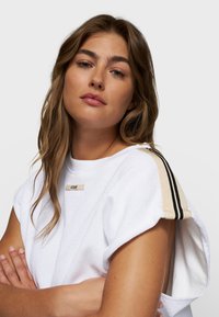 Top blanco de manga corta con un acabado texturizado, que presenta un escote redondo y rayas beige con acentos negros en los hombros.