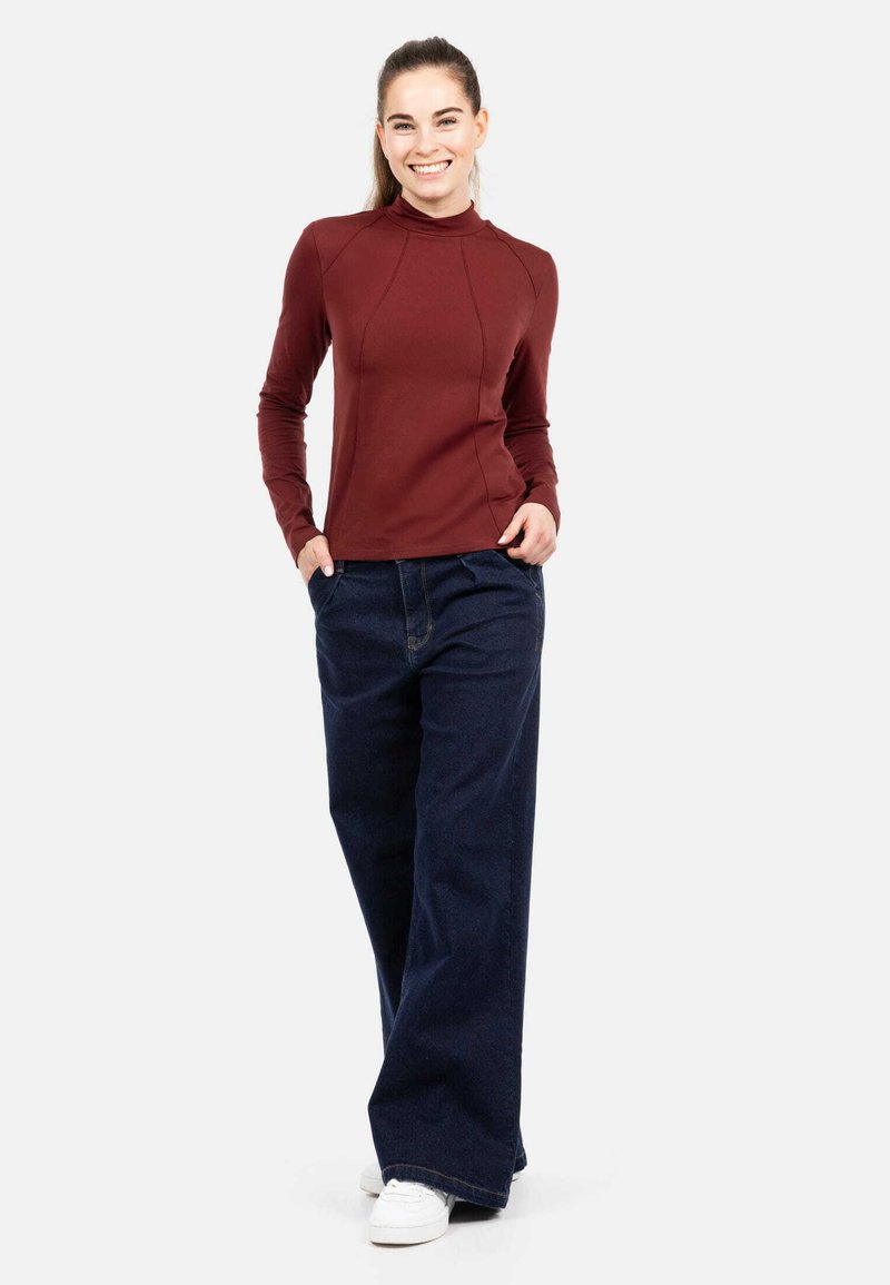 Pika varrukaga maroon värvi topp kõrge kraega, kombineeritud laia säärega tumedates sinistes teksades. Valged tennised täiendavad vabaaja outfiti.