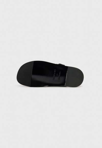 Suola di scarpa in pelle nera, texture liscia, forma arrotondata, marchio dettagliato stampato sulla superficie, con un leggero tacco e un design minimal.