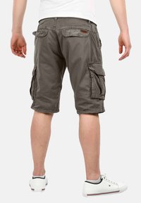Graue Cargo-Shorts mit mehreren Seitentaschen, knielang, aus strukturiertem Baumwollstoff. Getragen mit weißen Sneakers.