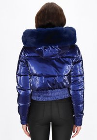 Błyszcząca niebieska kurtka puchowa z kapturem obszytym sztucznym futrem, ściągaczami na mankietach i na dole. Posiada pionowy pikowany wzór oraz boczne kieszenie.