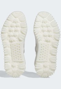 Soli de adidași albi texturati cu modele distincte de tracțiune, având elemente ridicate și secțiuni perforate pentru aderență și ventilație.