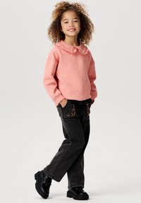 Ljusrosa sweatshirt med volangkrage, kombinerad med svarta jeans med blommig brodyr. Avslutas med svarta klumpiga stövlar.