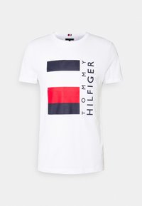 Camiseta blanca de algodón con un diseño gráfico que presenta franjas rectangulares en azul marino, rojo y blanco, y el logo "Tommy Hilfiger" en negro.