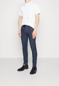 Vit kortärmad t-shirt med en liten logotyp, kombinerad med mörkblå slim-fit jeans och svarta ankle boots med texturerade sulor.