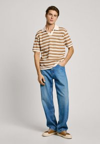 Striped polo shirt in orange, cream, and blue, with a collar and short sleeves; paired with light blue loose-fitting jeans and brown sneakers.