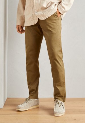 Khaki pants, cotton blend, slim fit, smooth texture. Paired with light grey suede shoes featuring laces and a crepe sole.