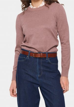 Lichtroze gebreide trui met lange mouwen en ribbels aan de manchetten, gedragen over donkerblauwe high-waisted jeans, geaccentueerd met een bruine leren riem.