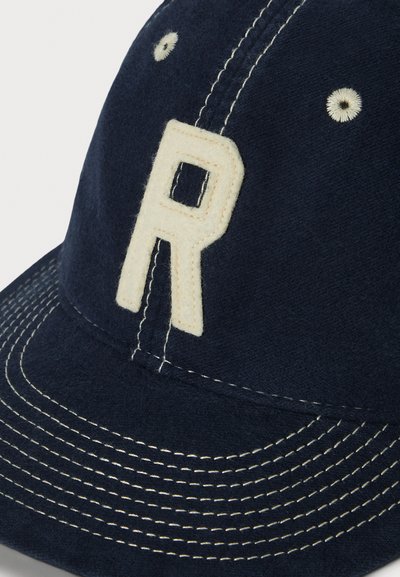 Kapica temno modre barve iz mehke tkanine z teksturirano površino. Ima kremno bel logotip »R« in kontrastne šive na šiltu.