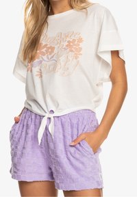 Weißes Baumwoll-T-Shirt mit pastellfarbigem Blumenmuster, kombiniert mit strukturierten lavendelfarbenen Shorts mit Bindebund und seitlichen Taschen.