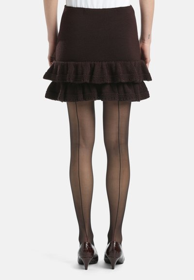 Brauner Strickrock mit volantsäum, kombiniert mit transparenten schwarzen Strumpfhosen mit einer vertikalen Naht und glänzenden burgunderfarbenen Absätzen.