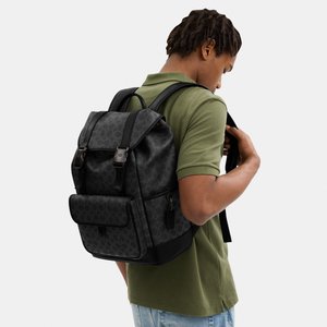 Mladi muškarac nosi crni kožni ruksak s uzorkom, prednjim džepom i remenima sa kopčama, odjeven u zelenu polo majicu i svijetloplave traperice.