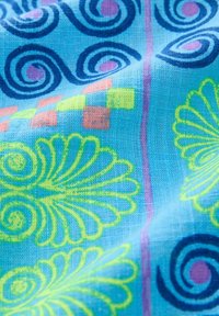 Tissu coloré avec un fond bleu orné de motifs tourbillonnants, de dessins floraux jaunes et roses vifs, et d'accents en damier. Tissage texturé.