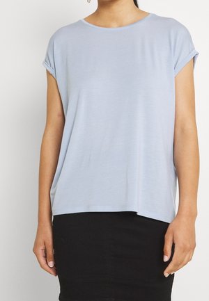 Femme portant un chemisier bleu clair à manches courtes et une jupe noire, vue des épaules aux hanches sur un fond uni.