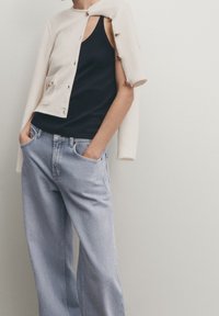 White knitted cardigan worn over a black tank top, paired with light blue wide-leg jeans. Cardigan features buttons and a partially open design.