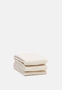 Medvilniniai rankšluosčiai, sukrauti į krūvą, kremine spalva, pasižymintys tekstūruota austine struktūra, apdailintais kraštais ir minkštu, sugeriančiu paviršiumi.