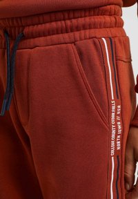 Röd sweatshirttyg med texturerad yta, med sidostripes i vit, blå och röd. Elastisk midja med dragsko.