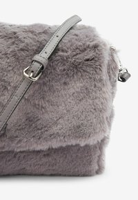 Sac d'épaule en fausse fourrure grise avec une surface texturée. Doté d'une lanière en cuir gris et d'un matériel en argent, avec une forme rectangulaire.