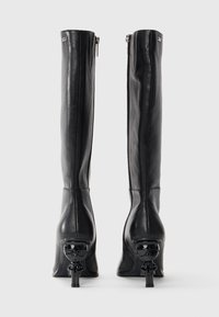 Black leather knee-high boots with a sleek design, pointed toes, and unique skull-shaped heel accents. Zipper closure at the back.