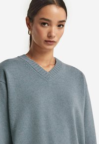 V-Ausschnitt, übergroßer Pullover aus weichem blauen Strickstoff. Mit geripptem Ausschnitt und Bündchen. Dezente Textur mit entspannter Silhouette.