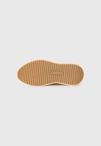 Rubber sole with horizontal grooves, tan color, slightly curved shape with a textured surface. Features the brand name embossed.