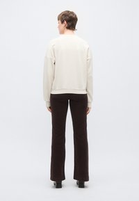 Φαρδιά ελαφρώς μπεζ φούτερ με ριμπ τελείωμα και μανσέτες, σε συνδυασμό με καφέ παντελόνι από κορντόρι με καμπάνα. Ομαλή υφή, ελάχιστες λεπτομέρειες σχεδίασης.