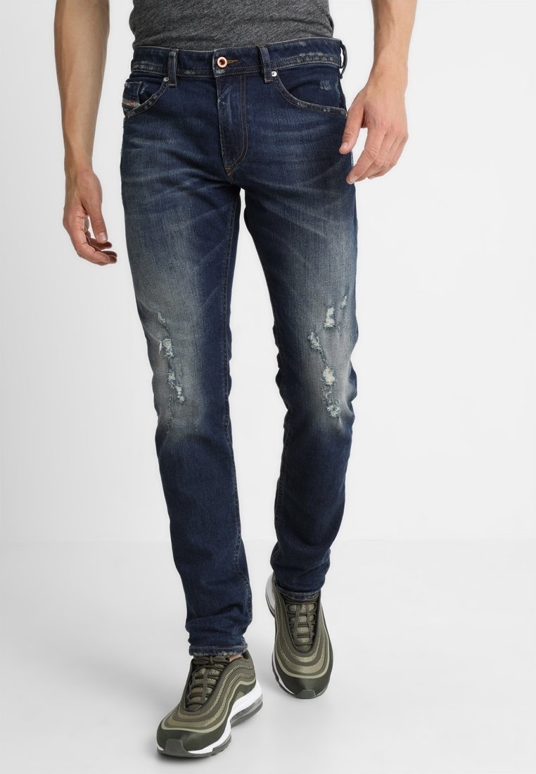 Jeans de mezclilla en azul oscuro con un acabado desgastado, detalles desgastados en los muslos, diseño clásico de cinco bolsillos y silueta ajustada.