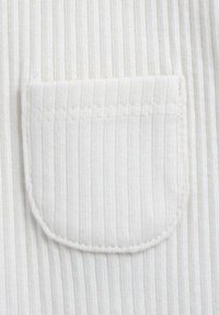 Tissu blanc à texture côtelée verticale avec une petite poche arrondie. Les coutures sont visibles et soigneusement finies le long des bords.