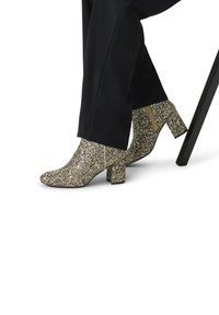 Glanzende gouden enkelboots met een spitse neus en blokhak. Voorzien van een zijrits en een sprankelende textuur op het bovenmateriaal.