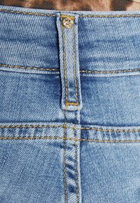 Los jeans de mezclilla azul claro presentan un diseño clásico con costuras amarillas, un botón de metal y una textura suave en la cinturilla.