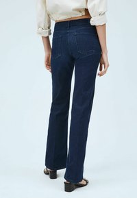 Tummansiniset suorat farkut, joissa on keskikorkea vyötärö. Farkuissa on kaksi takataskua ja hienovaraisia ompeluyksityiskohtia. Materiaali vaikuttaa olevan denimiä, jossa on vähäistä tekstuuria.