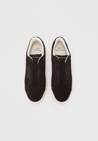 Black suede slip-on sneakers featuring elastic side panels and a white rubber sole. Crafted with minimalistic design and logo detailing.