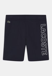 Marineblaue Baumwollshorts mit einem Logo-Patch auf dem linken Bein und einem auffälligen weißen "LACOSTE"-Schriftzug auf der rechten Seite. Glatte Textur mit elastischem Bund.